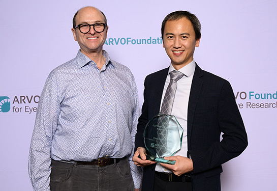 Two men stand next two each other against a lavender backdrop with the words “ARVO Foundation.” 