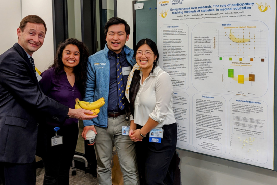 Jeff Hoch, associate director of CHPR, holds bananas with three first year medical students next to their research poster.