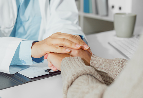 Health professional’s hands holding hands of patient in an office.
