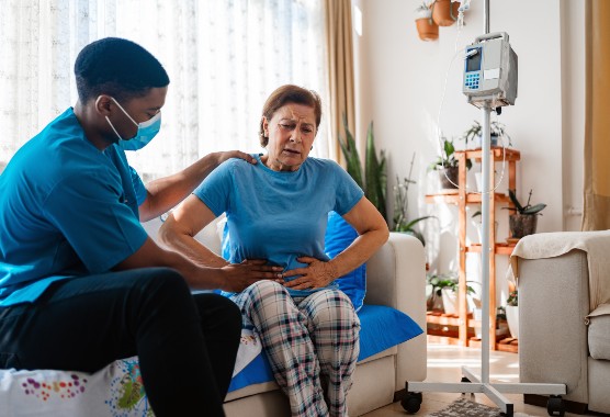 A mature woman with abdominal pain receiving a medical exam from a nurse in her home