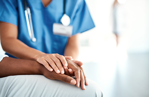 Close-up of a patient sitting down while a provider holds their hand reassuringly