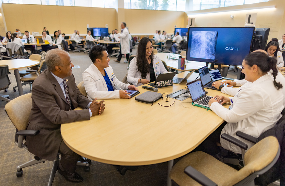 Chancellor Gary May, left, sits with four other students around a table all looking at a video monitor displaying an x-ray image.