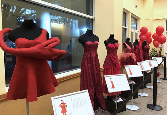 Five red dresses are displayed on mannequins and a bunch of red balloons in the background.