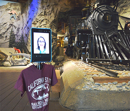 Woman walks next to two-wheeled robot with a video screen in museum.  