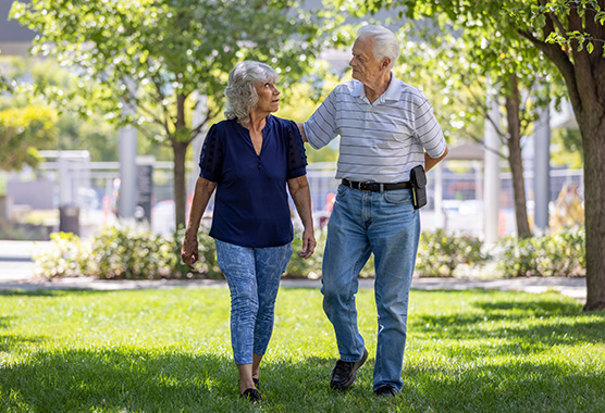 Older man walking in a park with his hand on his wife’s shoulder