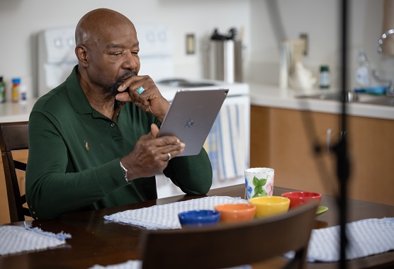 Man sitting at kitchen table looking serious while reading on a mobile tablet