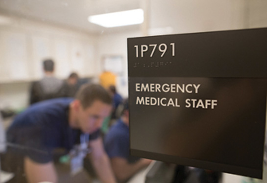 Door sign of Emergency Department office with doctor in background looking at computer