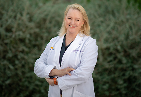 Woman with blonde hair in a white doctor’s coat smiling into camera