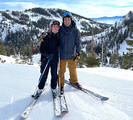 Man wearing ski apparel and helmet with his arm around young woman in similar attire.