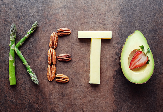 The word “Keto” word is spelled out with ketogenic food — asparagus, pecans, cheese and an half avocado.