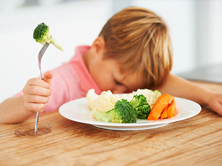 Blond kid sulks next to plate of veggies