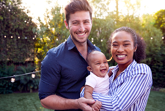 happy family of dad and mom holding baby, standing in backyard