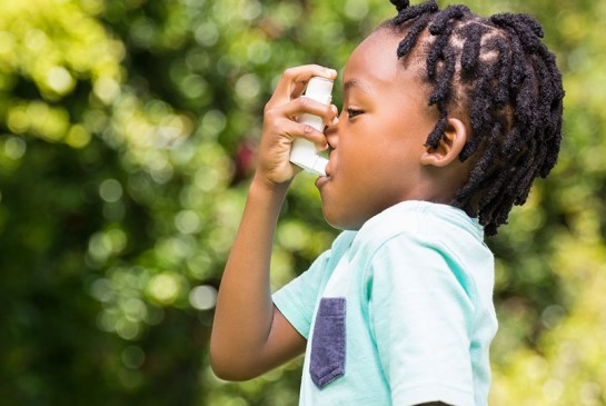 Young boy using inhaler in outdoor woodsy setting in background.
